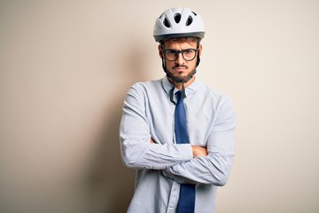 Young businessman wearing glasses and bike helmet standing over isolated white bakground skeptic and nervous, disapproving expression on face with crossed arms. Negative person.