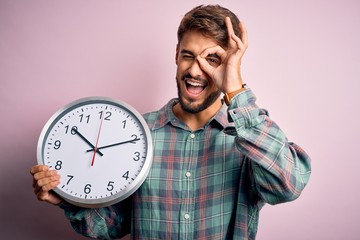 Young man with beard doing countdown using big clock over isolated pink background with happy face...