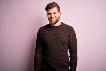 Obraz premium Young blond man with beard and blue eyes wearing casual sweater over pink background winking looking at the camera with sexy expression, cheerful and happy face.