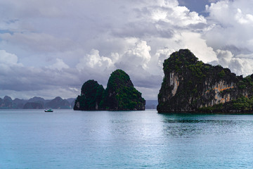 Fototapeta premium Daytime cloudy view of limestone pillars, calm water, and fisherman boat at Halong, Ha Long Bay, Vietnam