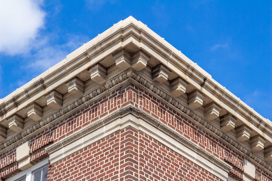 Upward view of the decorative roof cornice on a vintage red urban brick building, with blue sky background