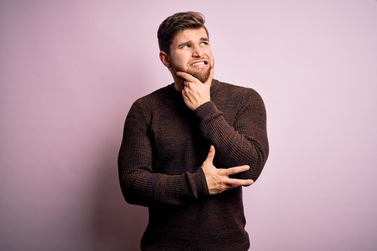 Young blond man with beard and blue eyes wearing casual sweater over pink background Thinking worried about a question, concerned and nervous with hand on chin