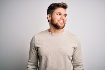 Young handsome blond man with beard and blue eyes wearing casual sweater looking away to side with smile on face, natural expression. Laughing confident.