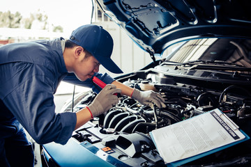 Car mechanic technician holding flashlight checking engine with checklist clipboard to maintenance...
