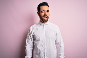 Obraz premium Young handsome man with beard wearing casual shirt standing over pink background winking looking at the camera with sexy expression, cheerful and happy face.