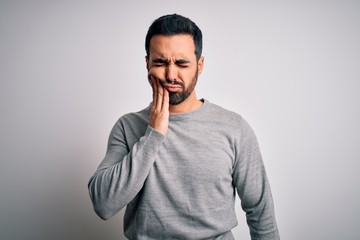 Young handsome man with beard wearing casual sweater standing over white background touching mouth with hand with painful expression because of toothache or dental illness on teeth. Dentist