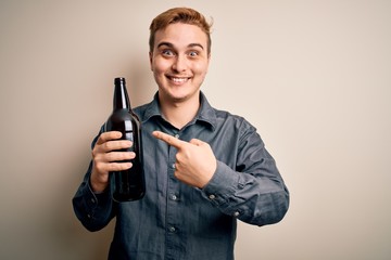 Young handsome redhead man drinking bottle of beer over isolated white background Smiling happy pointing with hand and finger