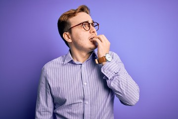 Young handsome redhead man wearing casual shirt and glasses over purple background looking stressed and nervous with hands on mouth biting nails. Anxiety problem.