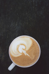 Close-up coffee latte art in cup and milk froth above to drink on wooden table background in the morning.
