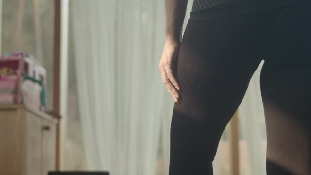 Woman stands in yoga pose indoors watching online class on laptop, tilt
