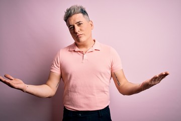 Young handsome modern man wearing casual pink t-shirt over isolated background clueless and confused expression with arms and hands raised. Doubt concept.