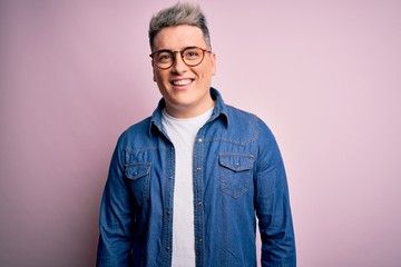 Young handsome modern man wearing glasses and denim jacket over pink isolated background with a happy and cool smile on face. Lucky person.