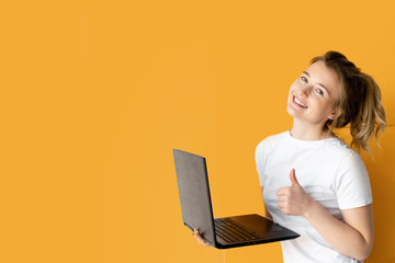 young beautiful woman in a white t-shirt with a laptop in her hands. Emotion of happiness and fun. A smile on his face. The thumb is up.