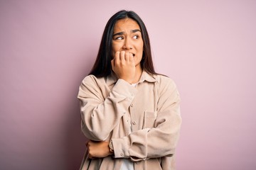 Young beautiful asian woman wearing casual shirt standing over pink background looking stressed and nervous with hands on mouth biting nails. Anxiety problem.