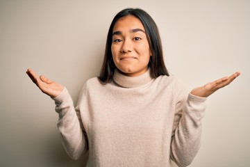 Young beautiful asian woman wearing casual turtleneck sweater over white background clueless and...