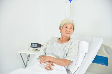 Lonely asian elderly female patient lying on the bed in the hospital ward and looking outside...