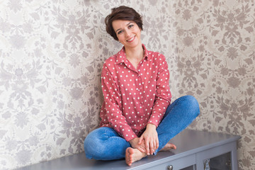 Girl sitting on chest of drawers at home.