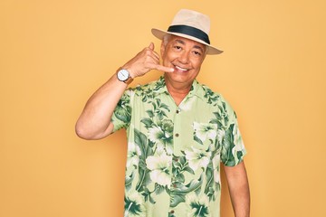 Middle age senior grey-haired man wearing summer hat and floral shirt on beach vacation smiling doing phone gesture with hand and fingers like talking on the telephone. Communicating concepts.