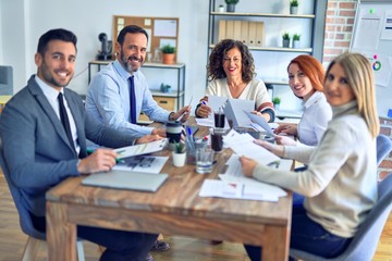 Fototapeta premium Group of business workers working together smiling happy. Sitting on desk posing with smile on face looking at the camera at the office