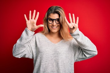Young beautiful blonde woman wearing sweater and glasses over isolated red background showing and...