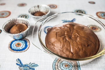 homemade chocolate cake and cupcakes on the table. round baked chocolate cake in glass baking bowl. Brown muffins in foiled baking forms