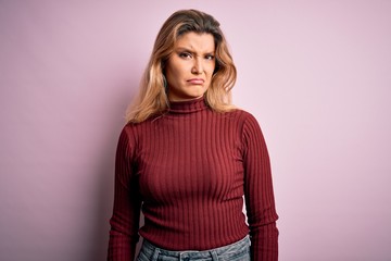 Young beautiful blonde woman wearing casual sweater over isolated pink background skeptic and...