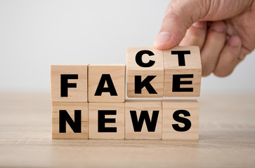 Hand flipping wooden cubic blocks for change "fake" to "fact" wording which is placed on "news"wording. It is fake news concept.
