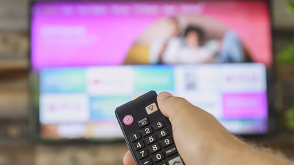 Male hand holding the TV remote control and changing TV channels