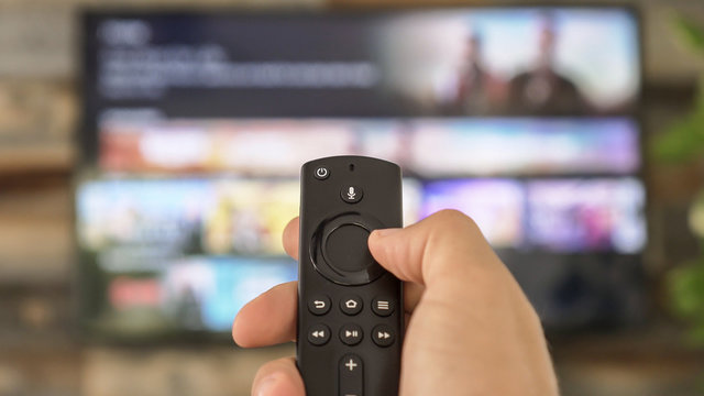 Male hand holding the TV remote control and changing TV channels
