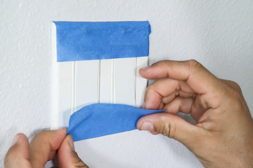 Painter Using Masking Blue Tape to Secure Light Switch. Preparation For Room