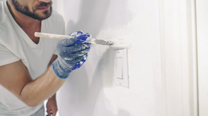 Close up of painter hands with gloves painting the wall edge with brush.