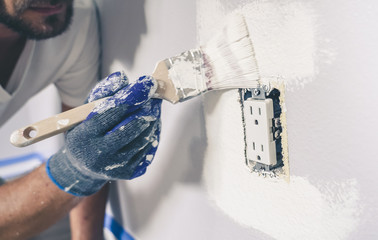 Painter man with gloves painting the wall around power outlet.