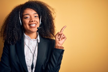 Young african american operator woman with afro hair wearing headset over yellow background with a...