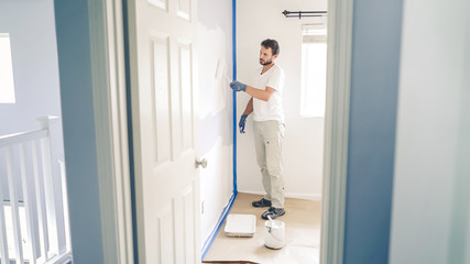 Painter man painting the wall in home, with paint roller and white color paint.