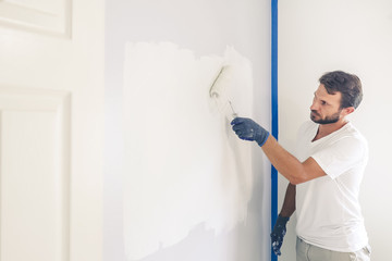 Painter man painting the wall in home, with paint roller and white color paint.