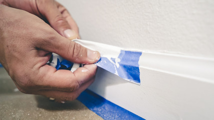 Painter Man Removing masking blue tape from molding, baseboard.