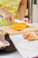 Housewife cutting carrot in thin slices with sharp knife when cooking dinner