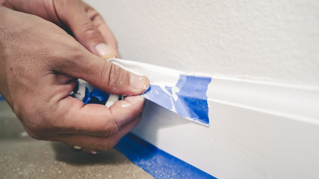 Painter Man Removing Masking Blue Tape From Molding, Baseboard.