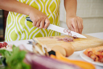 Housewife in apron cutting lotus stem in thin slices when cooking dinner