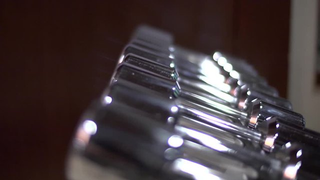 Many small weight in row in a gyms training room. The one handed weights are silver.