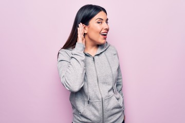 Young beautiful sporty woman wearing sportswear standing over isolated pink background smiling with hand over ear listening and hearing to rumor or gossip. Deafness concept.