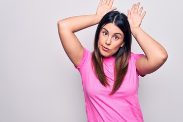 Fototapeta premium Young beautiful brunette woman wearing casual pink t-shirt standing over white background Doing bunny ears gesture with hands palms looking cynical and skeptical. Easter rabbit concept.
