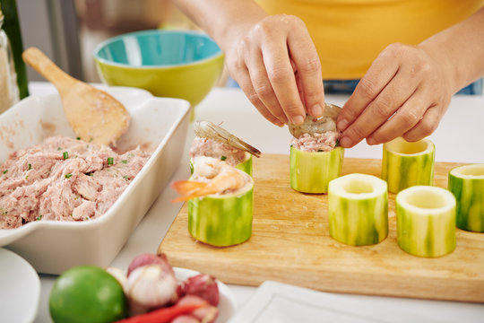 Close-up image of woman putting raw ground meet in zuccini rings and decorating it with shrimps