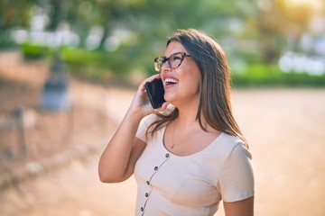 Fototapeta premium Young beautiful woman smiling happy and confident. Standing with smile on face talking by the smartphone at the city