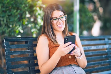 Young beautiful woman smiling happy and confident. Sitting with smile on face using smartphone at the city