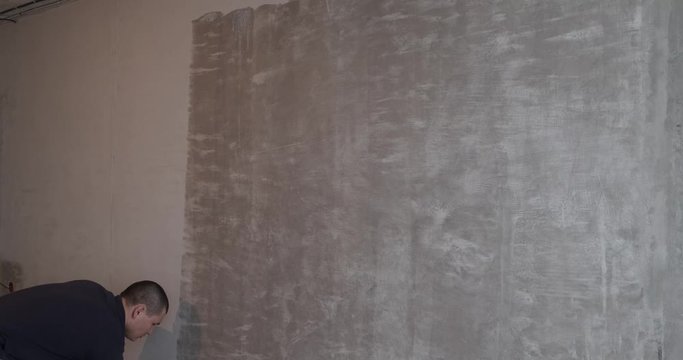 Painter applies special coating on concrete wall with roller, prepares walls for wallpapering, repairs in new apartment, methodical primer painting, painting, wall preparation, man at work, builder