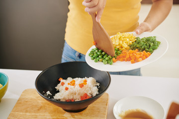 Woman cokking at home during covid19 quarantine and adding vegetables in bowl with boiled rice