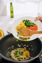 Woman frying vegetables like corn, carrot and pea in wok frying pan