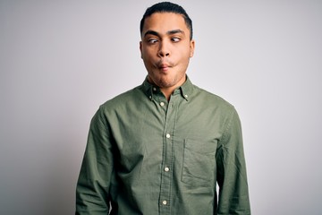 Young brazilian man wearing casual shirt standing over isolated white background making fish face with lips, crazy and comical gesture. Funny expression.