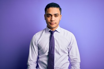 Young brazilian businessman wearing elegant tie standing over isolated purple background Relaxed with serious expression on face. Simple and natural looking at the camera.